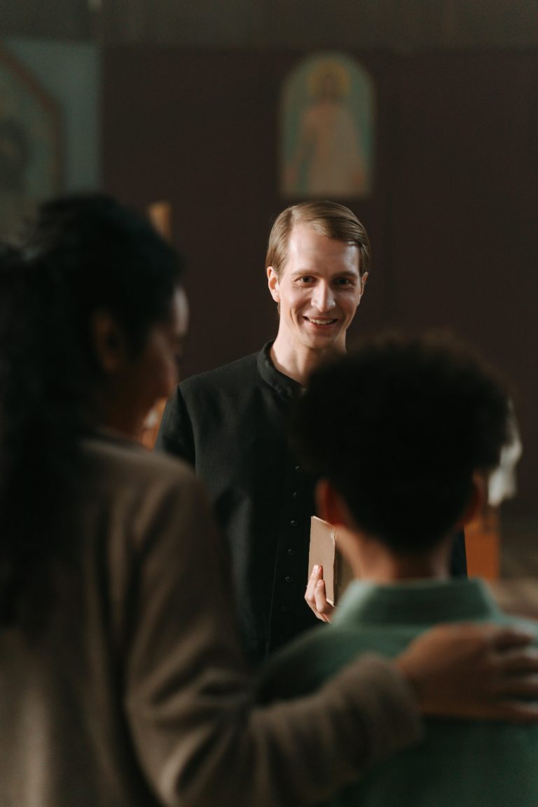 A smiling priest engages with parishioners in a church environment, exuding warmth and connection.