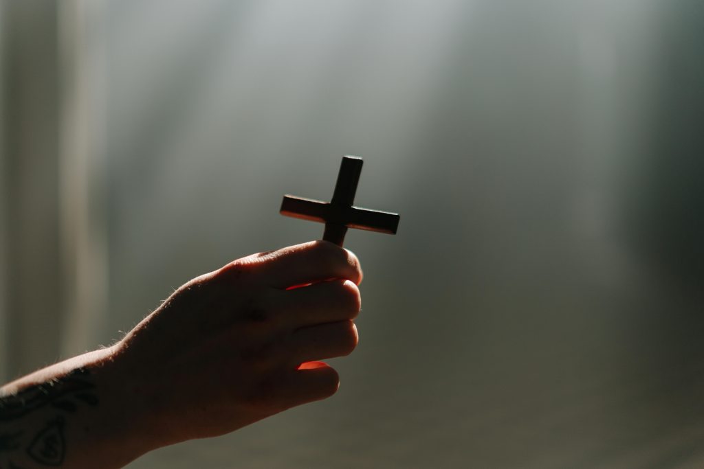 A hand holds a cross in a beam of light, symbolizing faith and spirituality.
